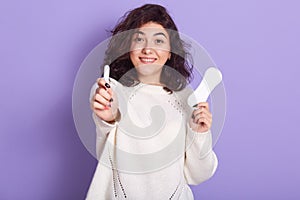 Portrait of cheerful attractive young lady holding tampon and sanitary napkin, making choices during menstruation, making photo