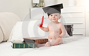 Portrait of cheerful baby boy in black graduating cap seating on