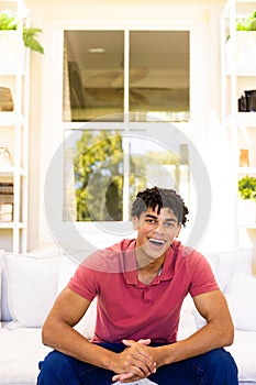 Portrait of cheerful biracial young man laughing while sitting on sofa in living room, copy space