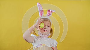 Portrait of cheerful blond little kid girl playing with easter egg on yellow background.