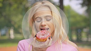 Portrait of cheerful blond woman biting sweet donut and laughing. Happy beautiful Caucasian lady eating delicious pastry