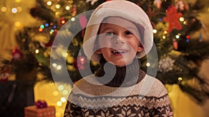 Portrait of cheerful boy smiling and laughing in camera next to Christmas tree at house. Families and children