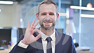 The Portrait of Cheerful Businessman showing Ok Sign in Office