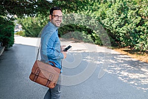 Portrait of cheerful businessman with smart phone walking on road at the city