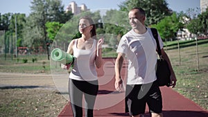 Portrait of cheerful caucasian couple strolling on running track after morning training. Happy man and woman talking and