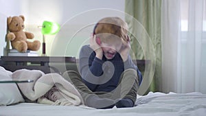 Portrait of cheerful caucasian little boy holding headphones with hands and singing. Redhead child listening to rock