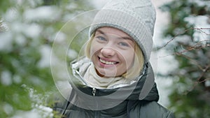 Portrait of cheerful charming young woman smiling looking at camera standing in fir forest outdoors on frosty day. Close