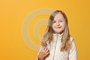 Portrait of a cheerful child in a beige jacket on a yellow background. Little girl blonde looks into the camera. Autumn concept.