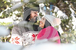Portrait of cheerful couple looking at each other and hugging in winter forest