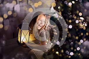 Portrait of a cheerful cute girl near a Christmas tree with a lantern. New Year holidays