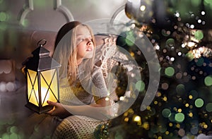 Portrait of a cheerful cute girl near a Christmas tree with a lantern. New Year holidays