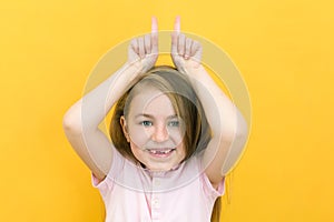 Portrait of cheerful cute little girl showing bull horn gesture, funny kid, joke. shooting indoors