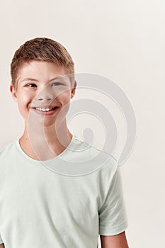 Portrait of cheerful disabled boy with Down syndrome smiling aside while posing isolated over white background