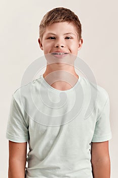 Portrait of cheerful disabled boy with Down syndrome smiling at camera while posing isolated over white background