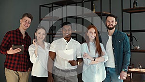 Portrait of cheerful diverse business team standing together in office, looking at camera.