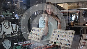 Portrait of cheerful female shop assistant demonstrating necklace made of rhodonite stone