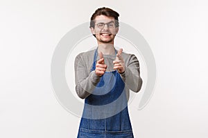 Portrait of cheerful friendly man in apron, work at coffee shop or restraurant, show informal greeting sign finger