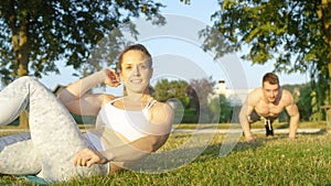 PORTRAIT: Cheerful girl does sit ups while happy boyfriend does push ups in park