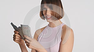 Portrait of cheerful girl happily counting money on camera over white background. Carefree girl