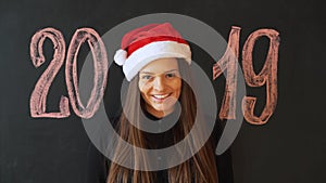 Portrait of a cheerful girl in Santa`s hat, against a black slate wall. Happy New Year 2019 Concept