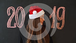 Portrait of a cheerful girl in Santa`s hat, against a black slate wall. Happy New Year 2019 Concept