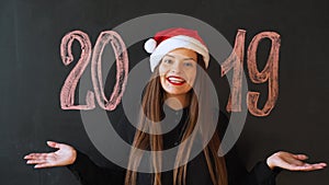 Portrait of a cheerful girl in Santa`s hat, against a black slate wall. Happy New Year 2019 Concept