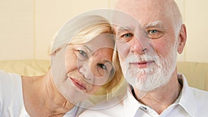 Portrait of cheerful good-looking senior couple sitting on sofa at home. Having good time relaxing.