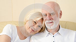 Portrait of cheerful good-looking senior couple sitting on sofa at home. Having good time relaxing.