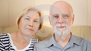 Portrait of cheerful good-looking senior couple sitting on sofa at home. Having good time relaxing.