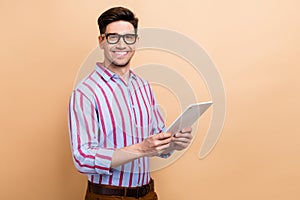 Portrait of cheerful guy business assistant using wireless tablet searching information in internet isolated on beige