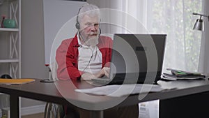 Portrait of cheerful handicapped senior man waving at laptop video chat smiling and talking in slow motion. Happy