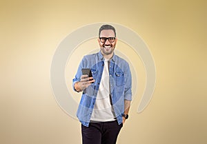 Portrait of cheerful handsome entrepreneur with hand in pocket messaging online over smart phone. Happy young man dressed in blue