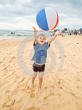 Portrait of cheerful happy smiling toddler boy throwing up and jumping with inflatable beach ball