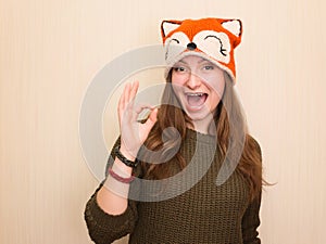 Portrait of a cheerful hipster girl in funny fox hat showing okay gesture