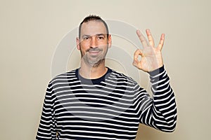 Portrait of a cheerful hispanic man showing ok gesture isolated on beige background.