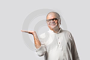 Portrait of cheerful Indian senior old man pointing or presenting or in hands folded pose