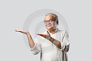 Portrait of cheerful Indian senior old man pointing or presenting or in hands folded pose