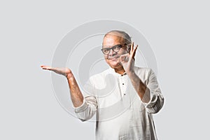 Portrait of cheerful Indian senior old man pointing or presenting or in hands folded pose