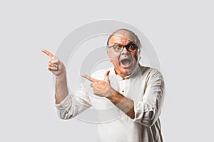 Portrait of cheerful Indian senior old man pointing or presenting or in hands folded pose