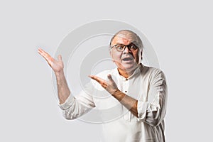 Portrait of cheerful Indian senior old man pointing or presenting or in hands folded pose