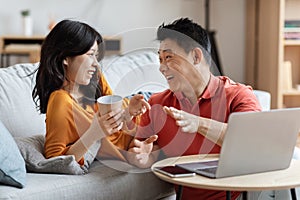 Portrait of cheerful korean spouses using laptop together, having conversation