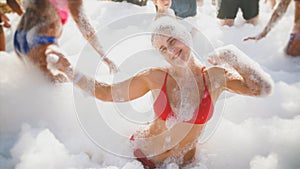 Portrait of cheerful laughing woman dancing and having fun on the soap foam disco party at sea beach