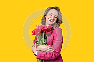 Portrait of cheerful laughing woman in suit holding bunch of tulips over yellow background