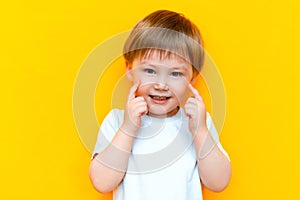 Portrait of cheerful little boy child three years old, standing isolated over yellow background. Looking camera. showing white