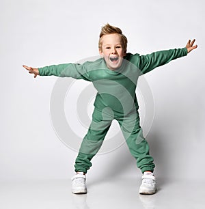 portrait of a cheerful little boy dressed in a green tracksuit. Cute baby posing on a white background - shouts with joy