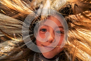 Portrait of a cheerful little girl with her hair flying in the wind and sun. Bottom view. A cute child looks down. Children`s