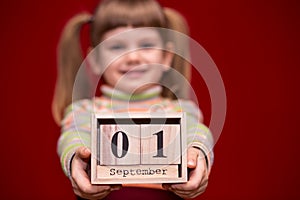 Portrait of cheerful little girl isolated on red hold wooden calendar set on first september