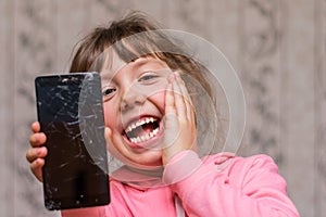 Portrait of a cheerful little girl with a mobile phone. The child broke the telephone communicator and laughs. Baby joked breaking