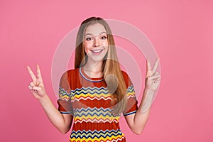 Portrait of cheerful lovely girl toothy smile demonstrate v-sign empty space isolated on pink color background