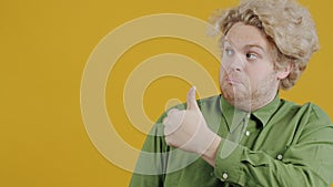 Portrait of cheerful male showing thumbs-up and pointing sidewards smiling on yellow background